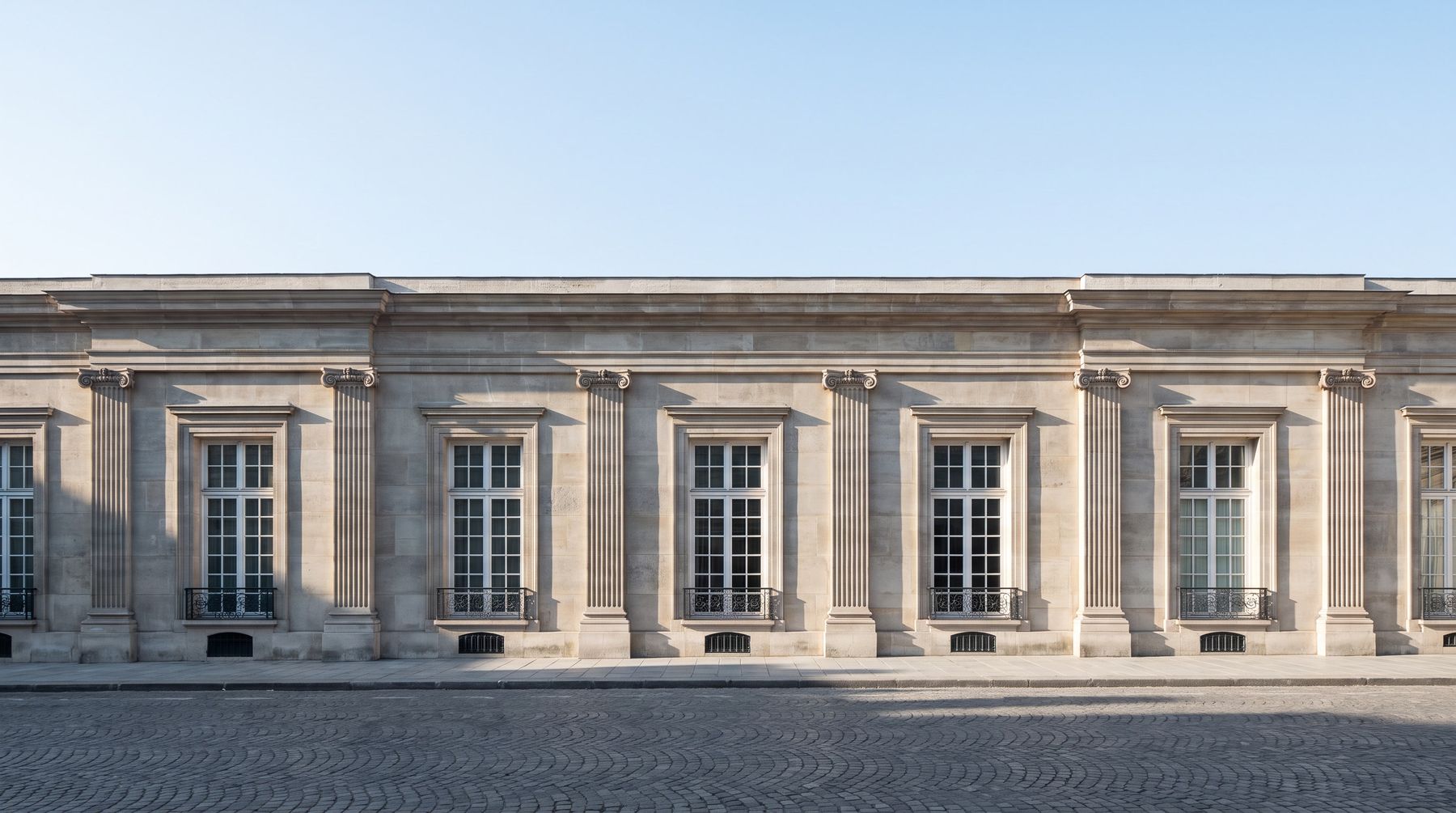La façade de pierre néoclassique en plein jour, pierre claire et ombres nettes.
