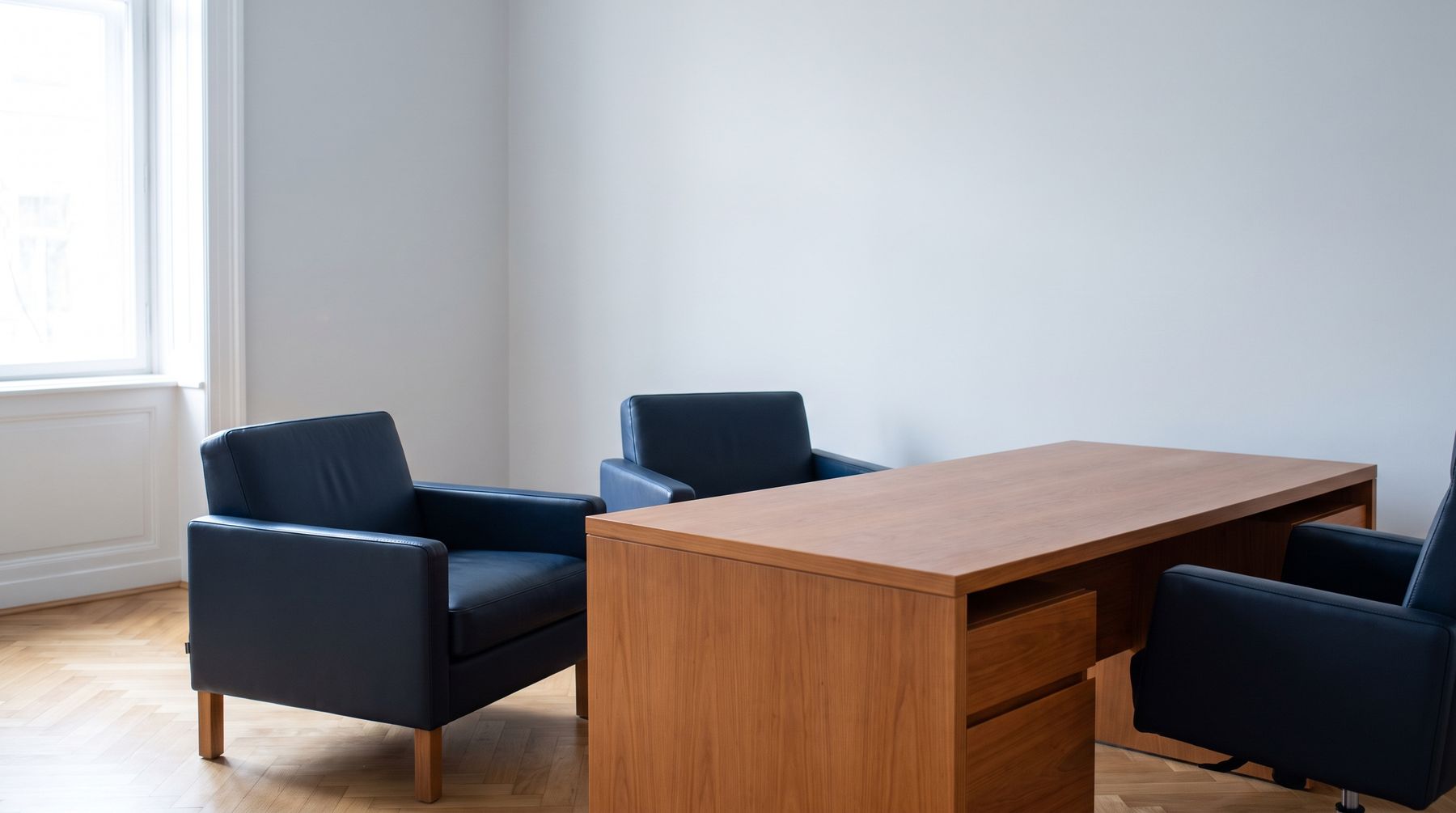 Deux fauteuils en cuir sombre face à un bureau, dans une pièce claire — le fauteuil visiteur est vide.