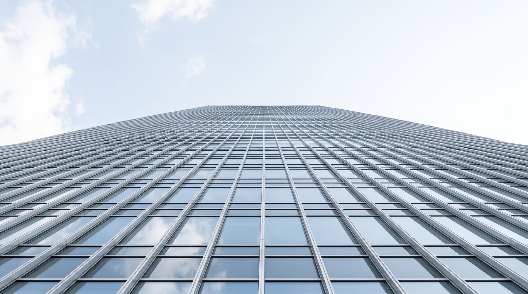 Façade vitrée d'un immeuble de bureaux contemporain, en contre-plongée, reflétant le ciel.