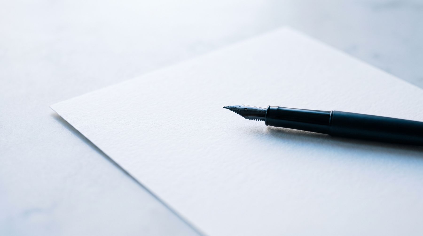 Une feuille de papier vierge et un stylo plume, sur une surface claire.